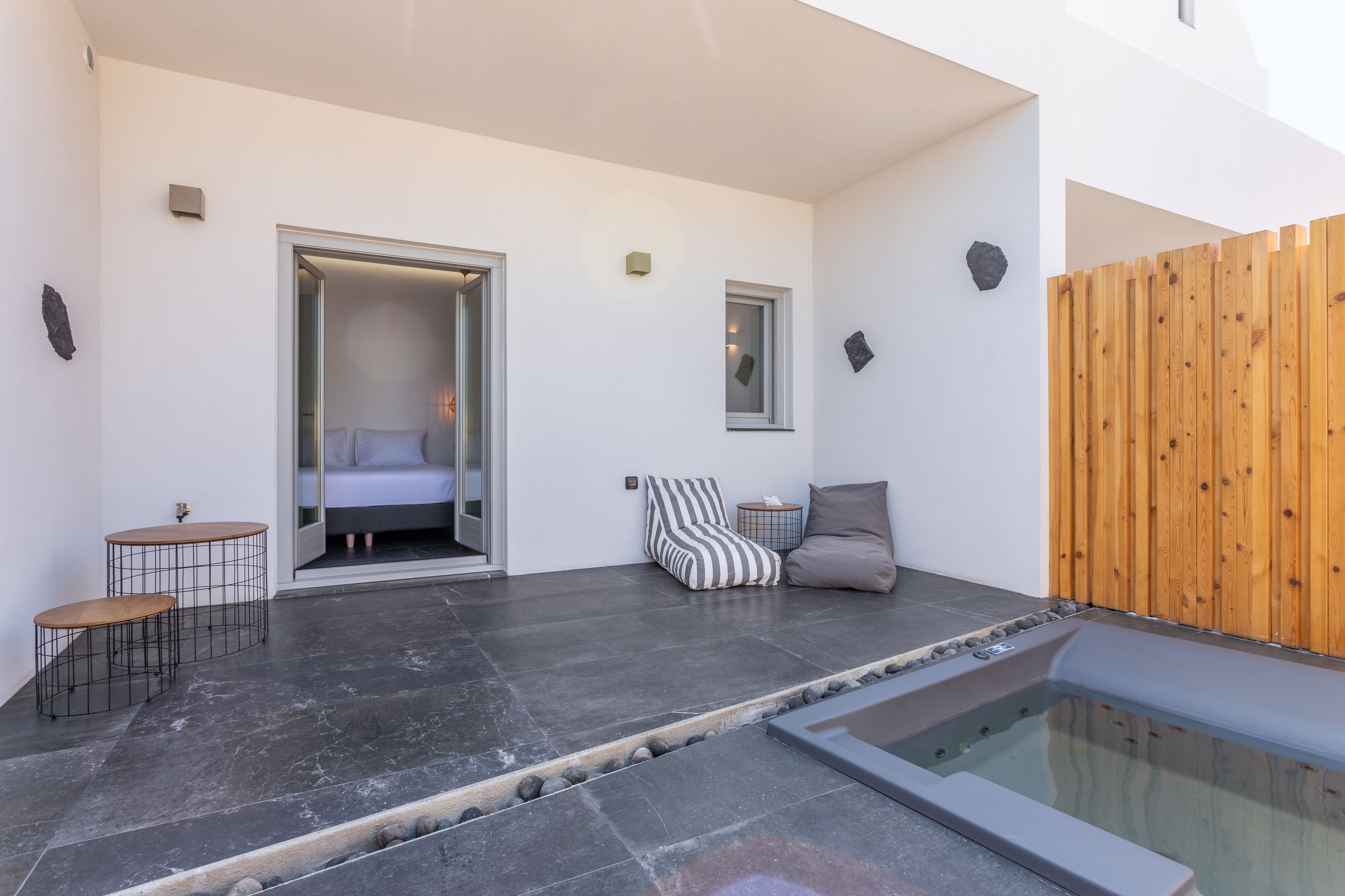 A modern outdoor living area with a hot tub, a seating area with cushions, and a small table.