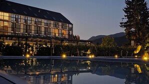 A modern building with a reflective pool, outdoor seating, and a mountain backdrop. - Lyra Hotel Plitvice (Plitvicka Jezera)