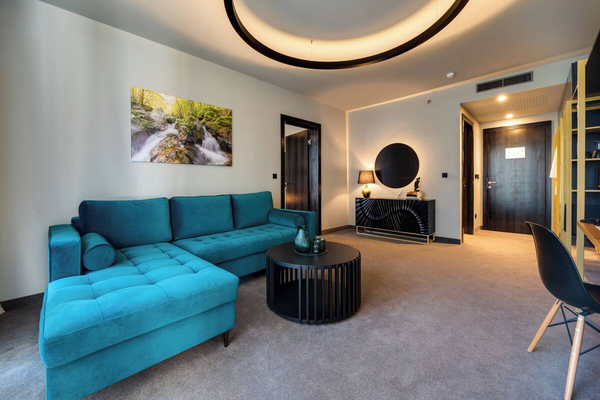 Una sala de estar moderna con un sofá color turquesa, una mesa de centro redonda y un cuadro de una cascada.