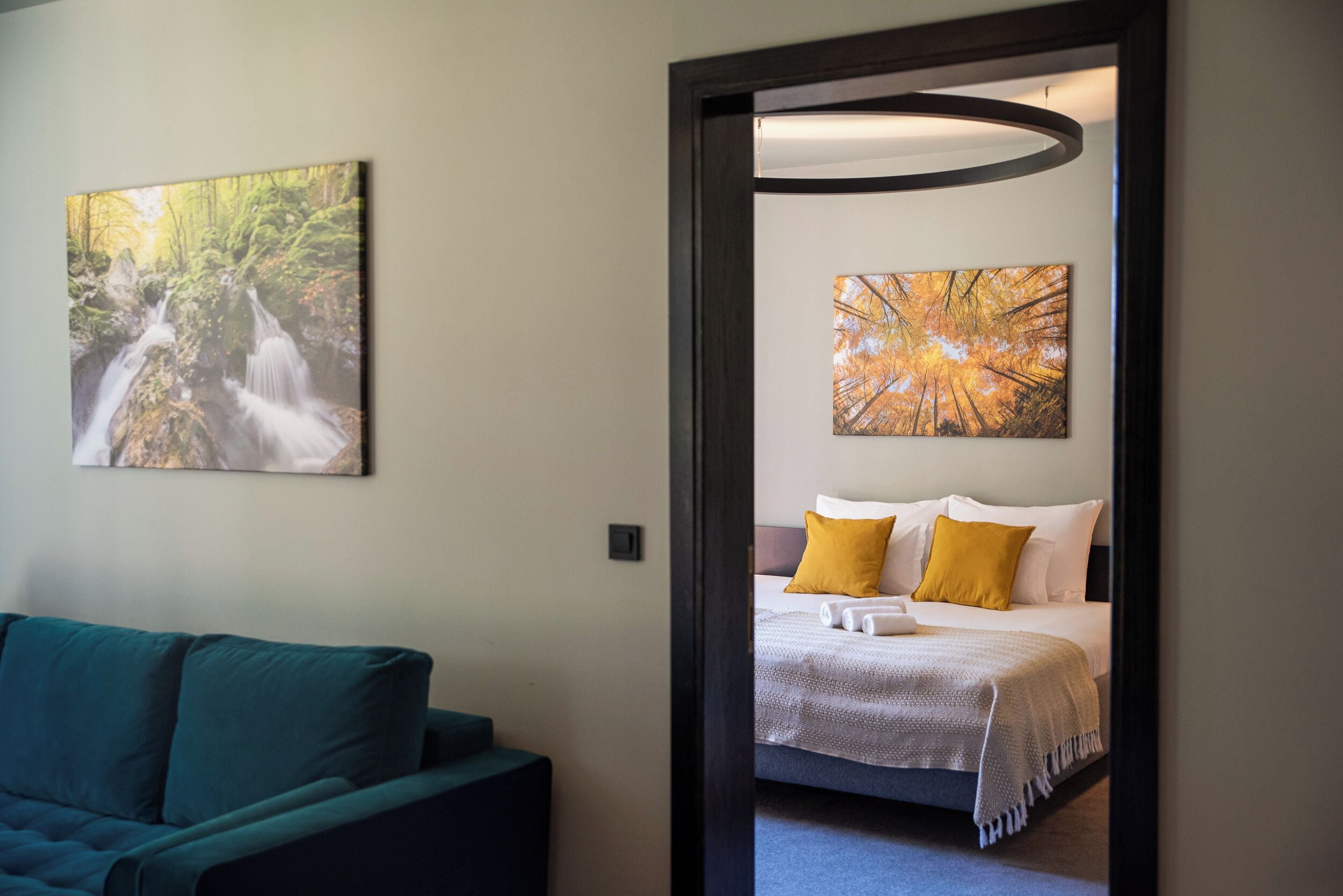 A hotel room with a bed, two pillows, a bedside table, and a painting of a waterfall.