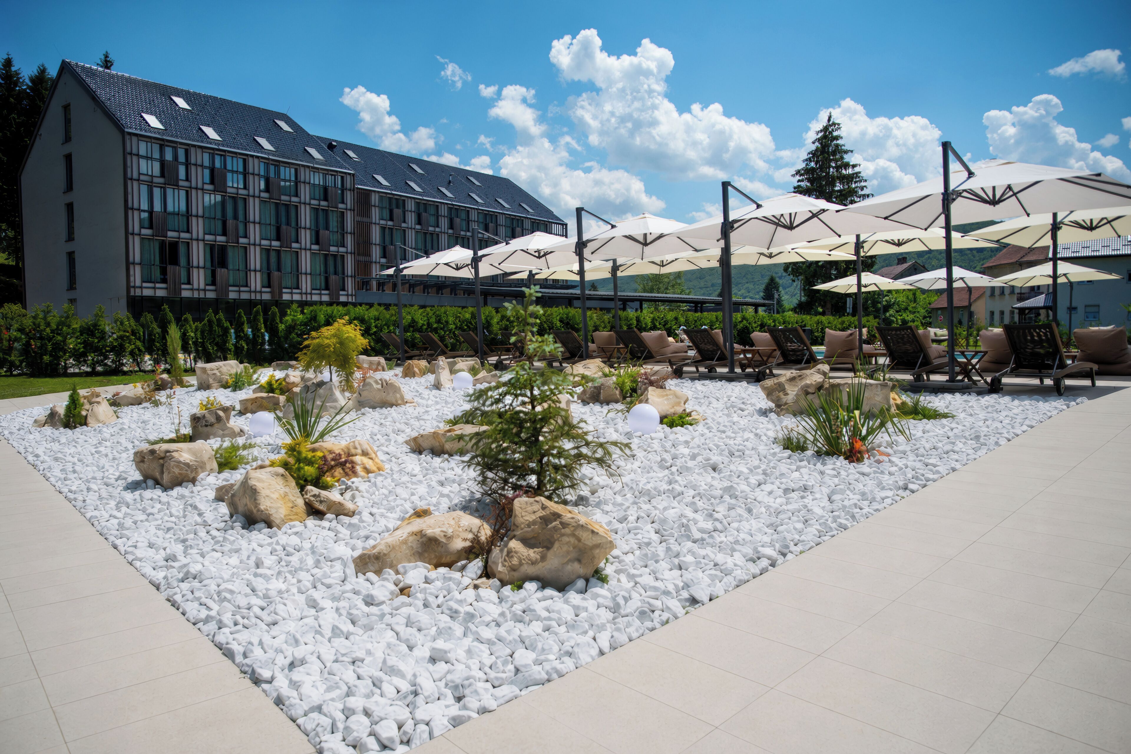 A modern outdoor seating area with white pebbles and rocks, surrounded by lounge chairs and umbrellas.