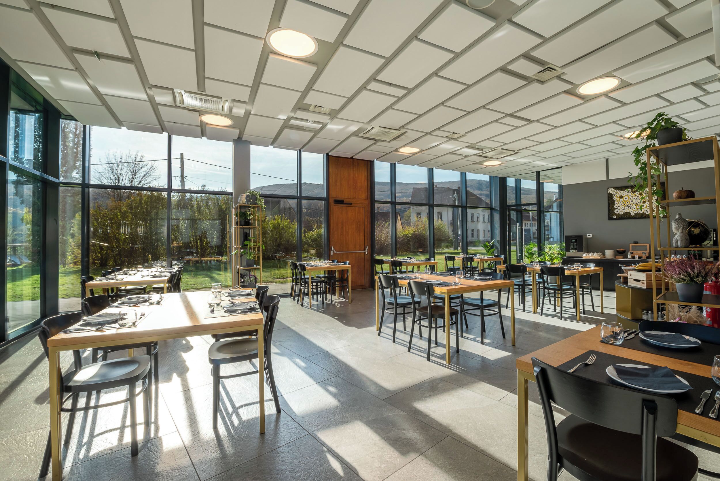 A spacious dining area with large windows, modern ceiling design, and neatly arranged tables and chairs.