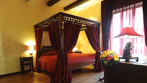 A four-poster bed with red curtains, a bedside table with a lamp, and a vase of flowers on a wooden nightstand. - Muro Torto Cairoli (Foggia)