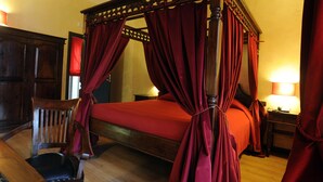 A four-poster bed with red curtains, a wooden chair, and a nightstand with a lamp. - Muro Torto Cairoli (Foggia)