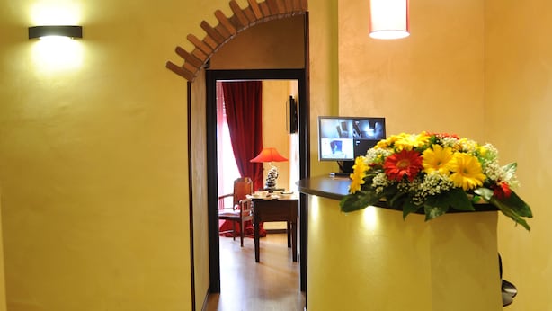 A hotel reception area with a wooden floor, a reception desk with a floral arrangement, a television screen, and a red curtain in the background. - Muro Torto Cairoli (Foggia)