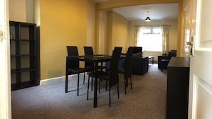 Un comedor con una mesa y sillas, una estantería, y vistas a una habitación con ventana y cortinas.