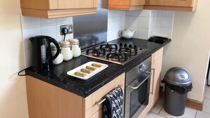 Una cocina con armarios de madera, una estufa a gas, un hervidor y un cubo de basura.