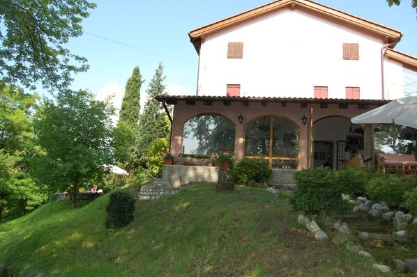 A two-story building with a white facade and red shutters, featuring large arched windows and a covered outdoor seating area. - B&B Four Winds (Follina)