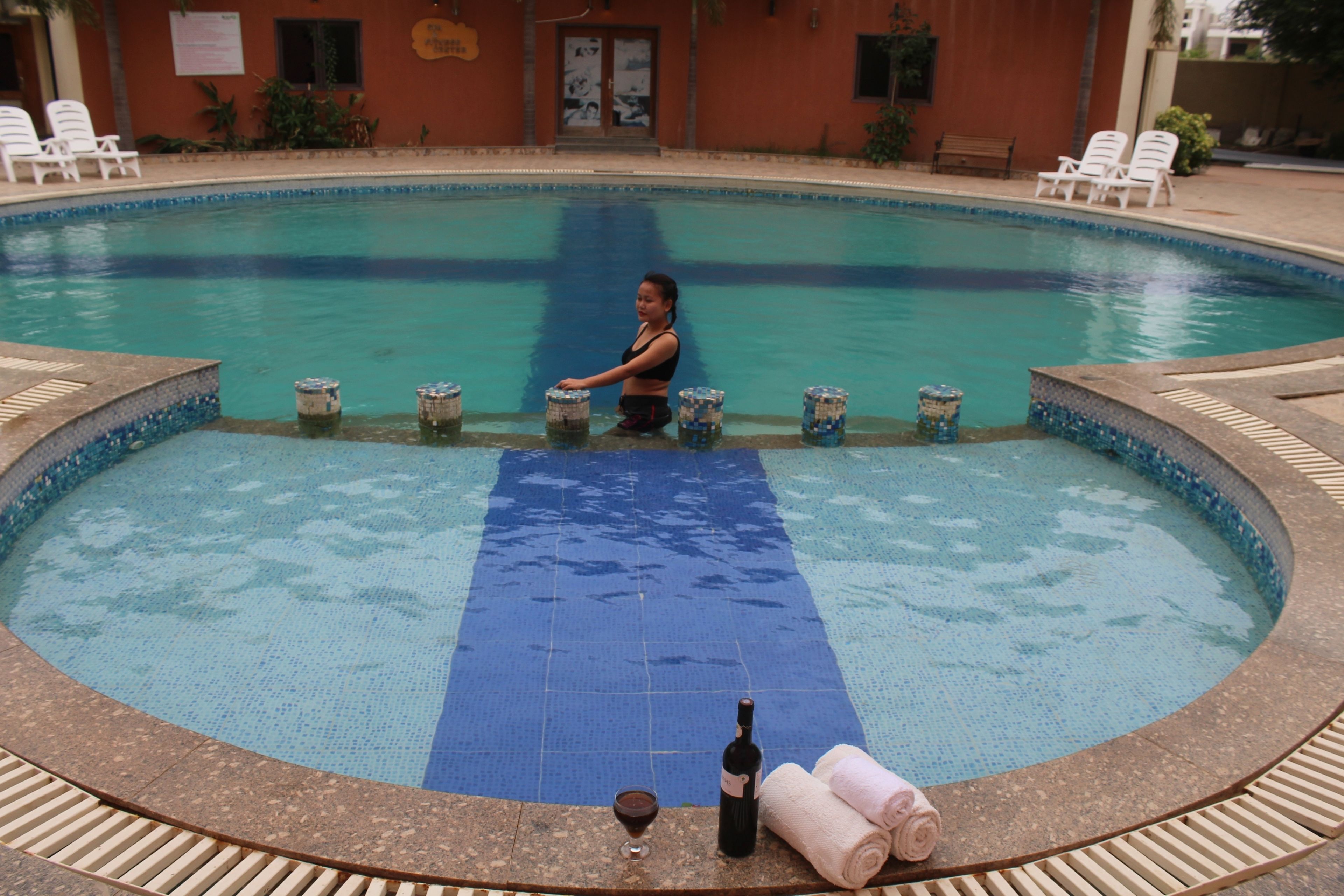 A pool with a blue mat, lounge chairs, and a bottle of wine.
