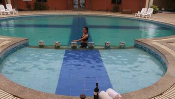 A pool with a blue mat, lounge chairs, and a bottle of wine.