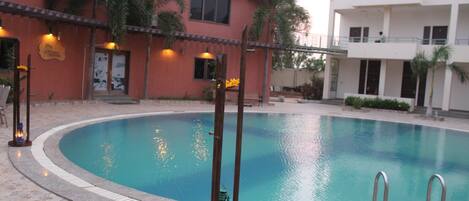 A swimming pool with a stone border, surrounded by a building with a red facade and palm trees.