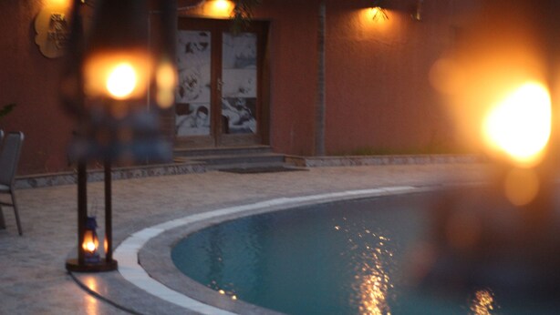 Una piscina con borde curvo, un pequeño elemento acuático y un edificio con fachada de azulejos al fondo.