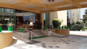 Entrada de hotel con fachada de vidrio, zona de estar al aire libre y una escalera que conduce a la entrada.