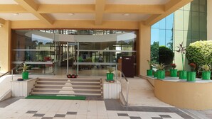 Una entrada de edificio moderna con puerta de vidrio, una escalera y plantas en macetas.