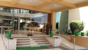 Un moderno vestíbulo de hotel con entrada de cristal, una escalera y plantas en macetas.