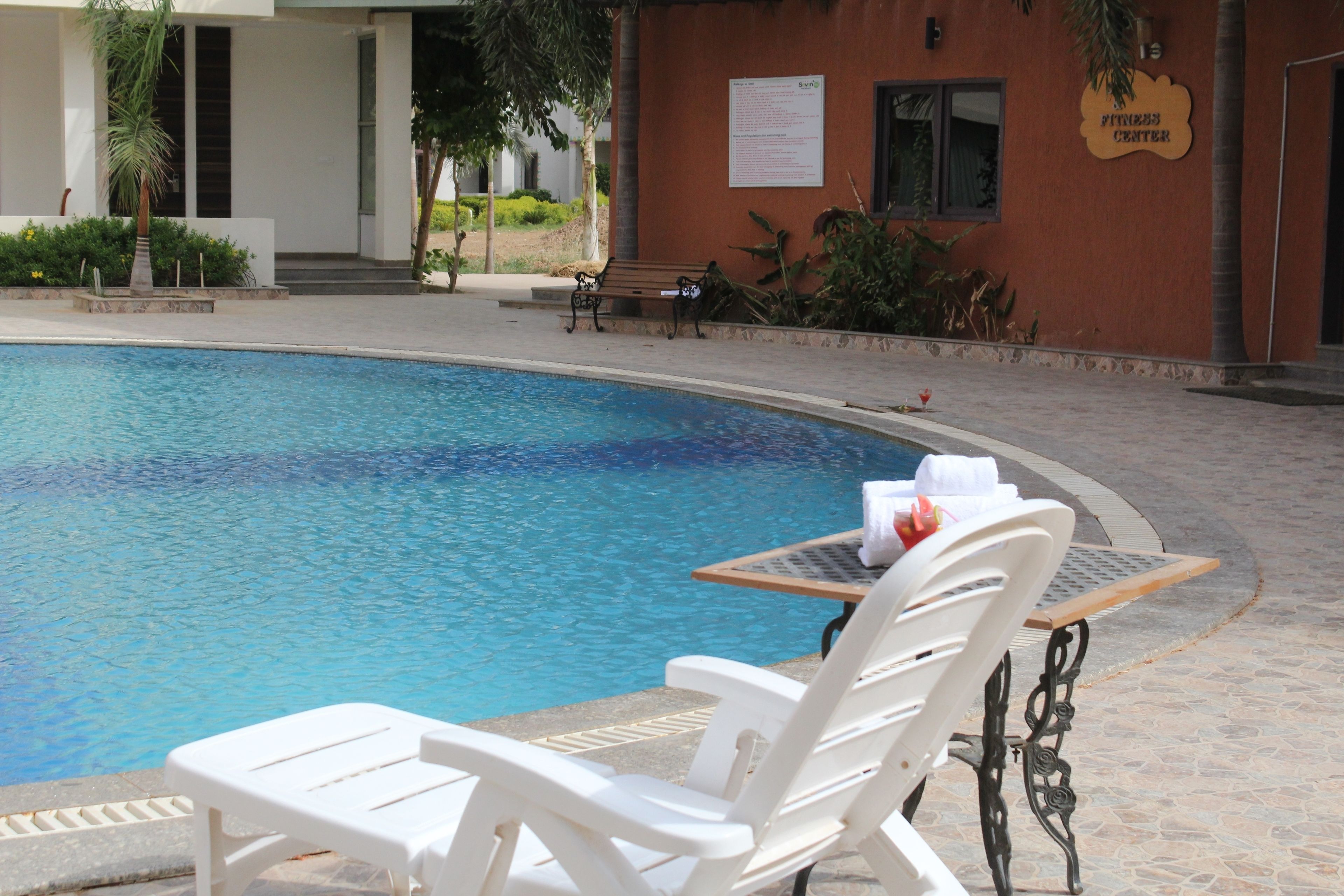 A swimming pool with lounge chairs and a table, a sign reading "Fitness Center", and a building entrance.