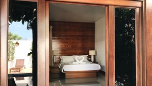 A bedroom with a wooden headboard, a bed with white linens, a bedside lamp, and a heart-shaped towel on the bed. - The Nest Samui (Koh Samui)