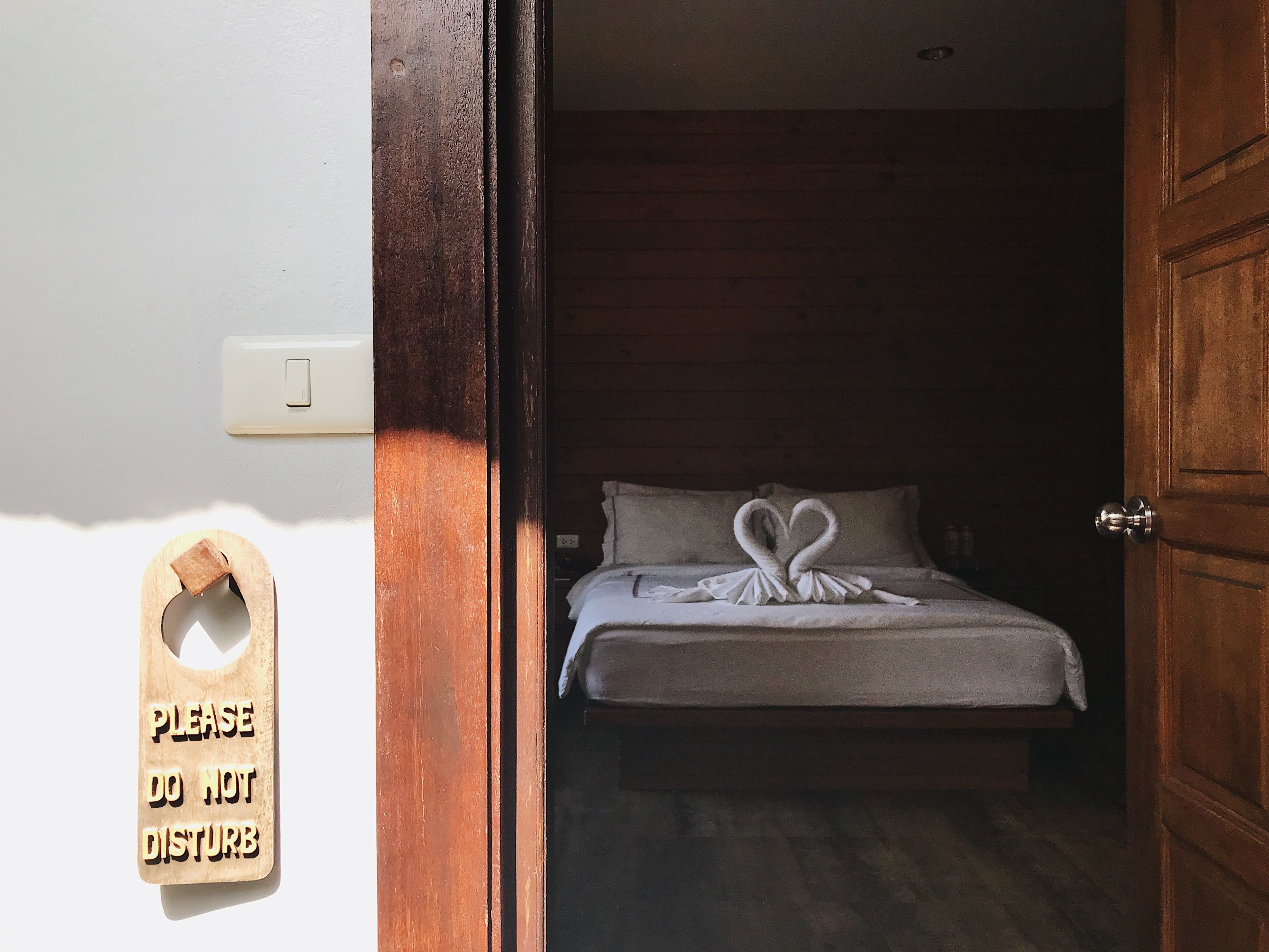 A hotel room with a bed, a wooden door, and a 'Please do not disturb' sign.