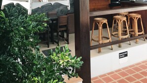A kitchen area with wooden cabinets, a sink, and a bar counter with stools. There are hanging light fixtures and a white birdcage with a bird inside. - The Nest Samui (Koh Samui)