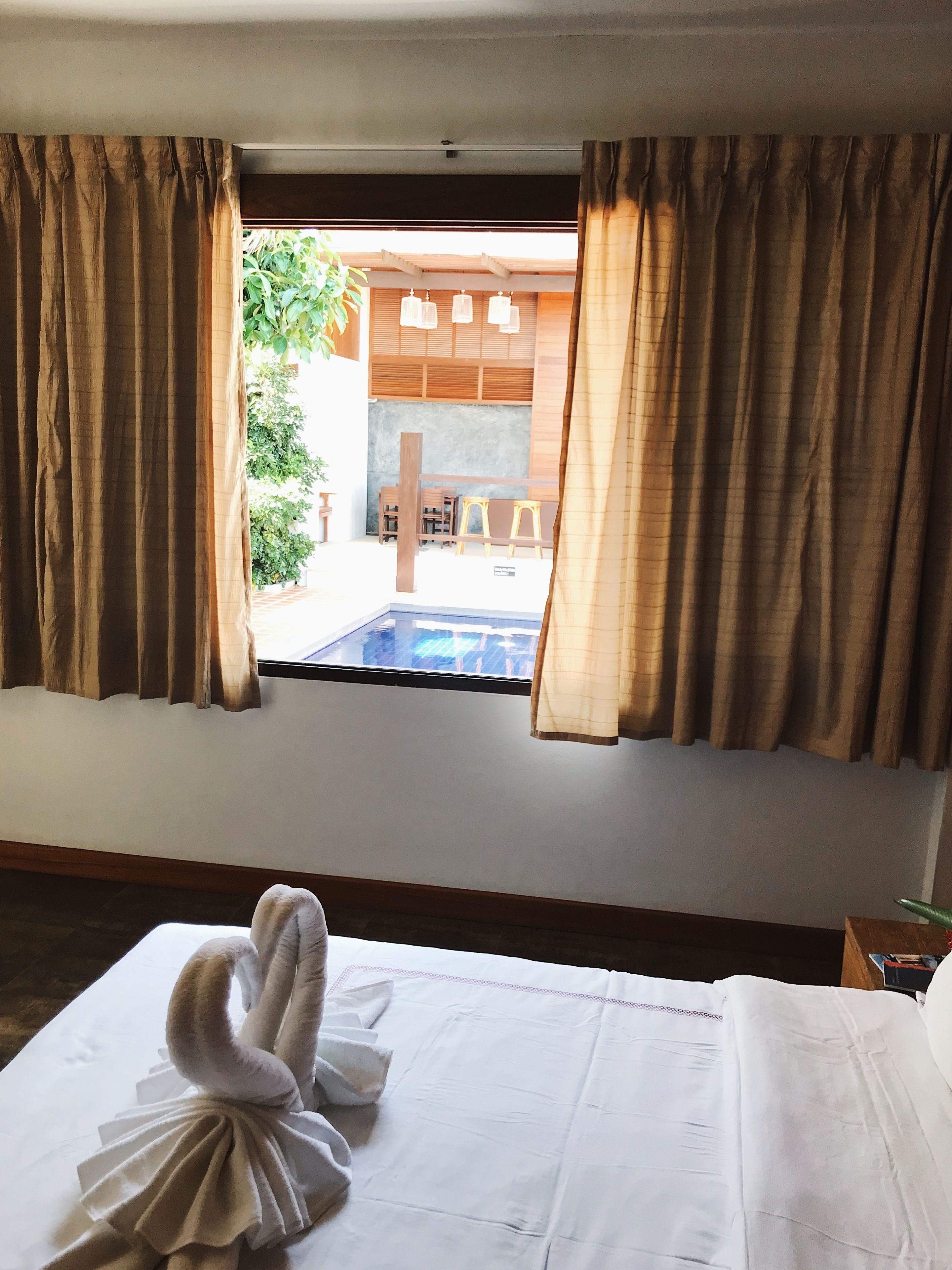 A hotel room with a bed, a window with curtains, and a view of an outdoor pool area.