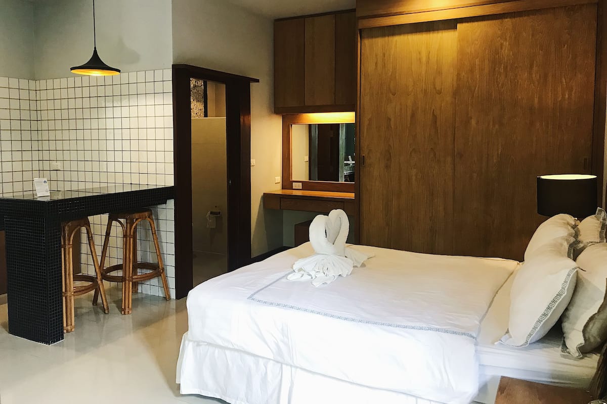 Una habitación de hotel con cama, escritorio con taburetes, espejo y armario de madera.