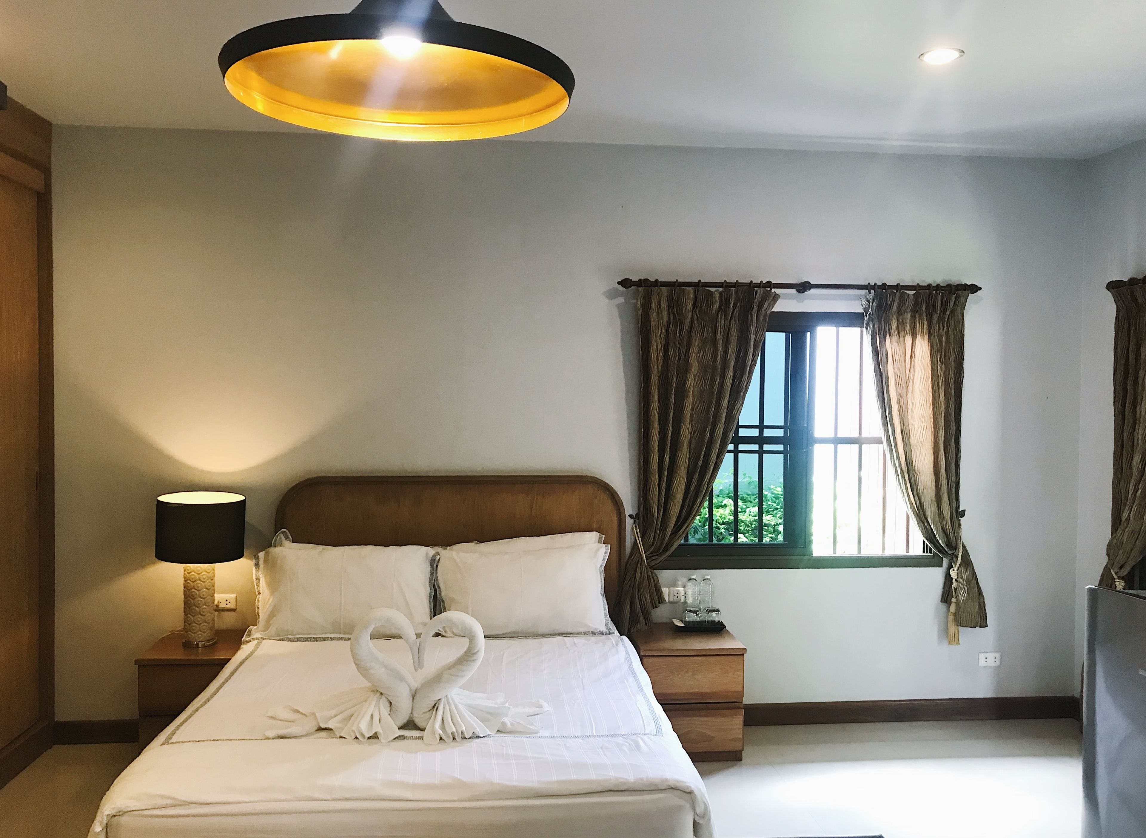 A hotel room with a bed, a bedside lamp, a window with curtains, and a ceiling light.