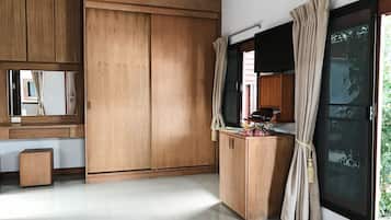 Una habitación con armarios de madera, un espejo, una mesita con flores y un ventanal con cortinas.