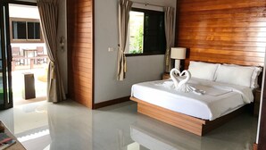 A modern hotel room with a large bed, wooden paneling, a window with curtains, a bedside table with a lamp, and a view of the outdoor area. - The Nest Samui (Koh Samui)