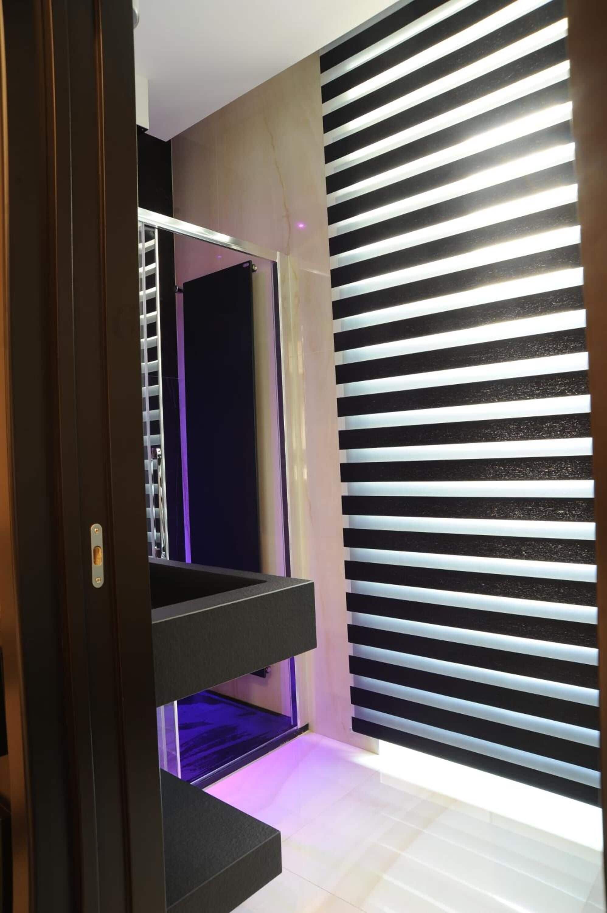 Un interior moderno con una escalera que baja a un nivel inferior, una pared con persianas horizontales y un marco de puerta visible.