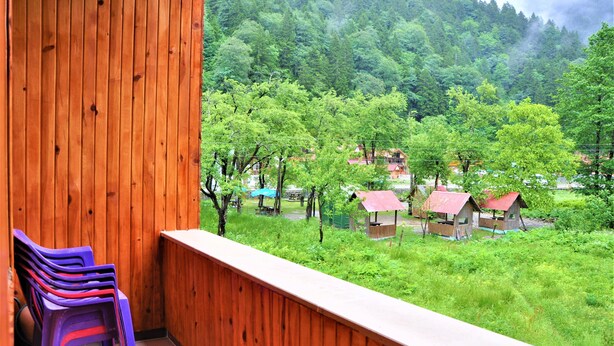 A balcony with wooden railings and purple plastic chairs, overlooking a lush green landscape with trees and small buildings. - Yaren Otel (Çaykara)