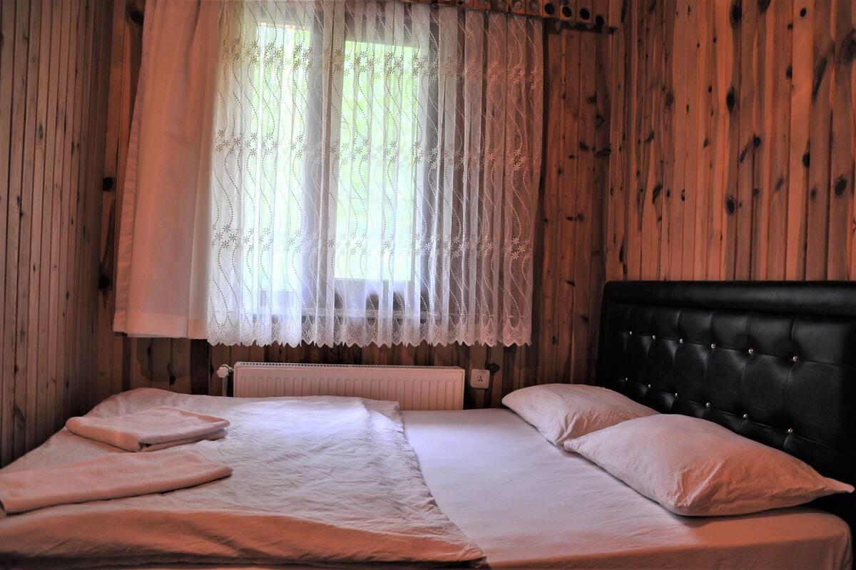 Un dormitorio con una cama doble, cabecera y ventana con cortinas traslúcidas.