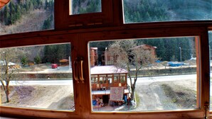 A wooden cabin with large windows overlooking a dirt road and a building with a red roof. - Yaren Otel (Çaykara)