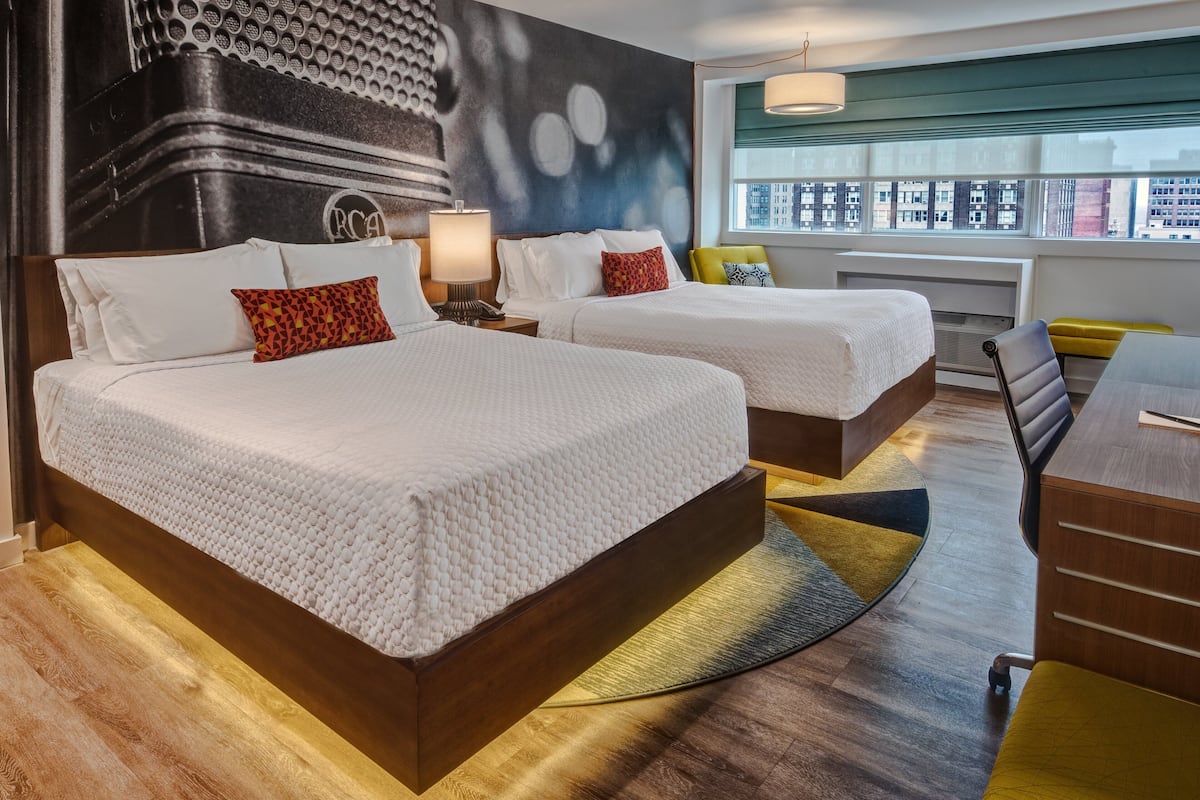 Habitación de hotel con dos camas, un escritorio y vistas a la ciudad.
