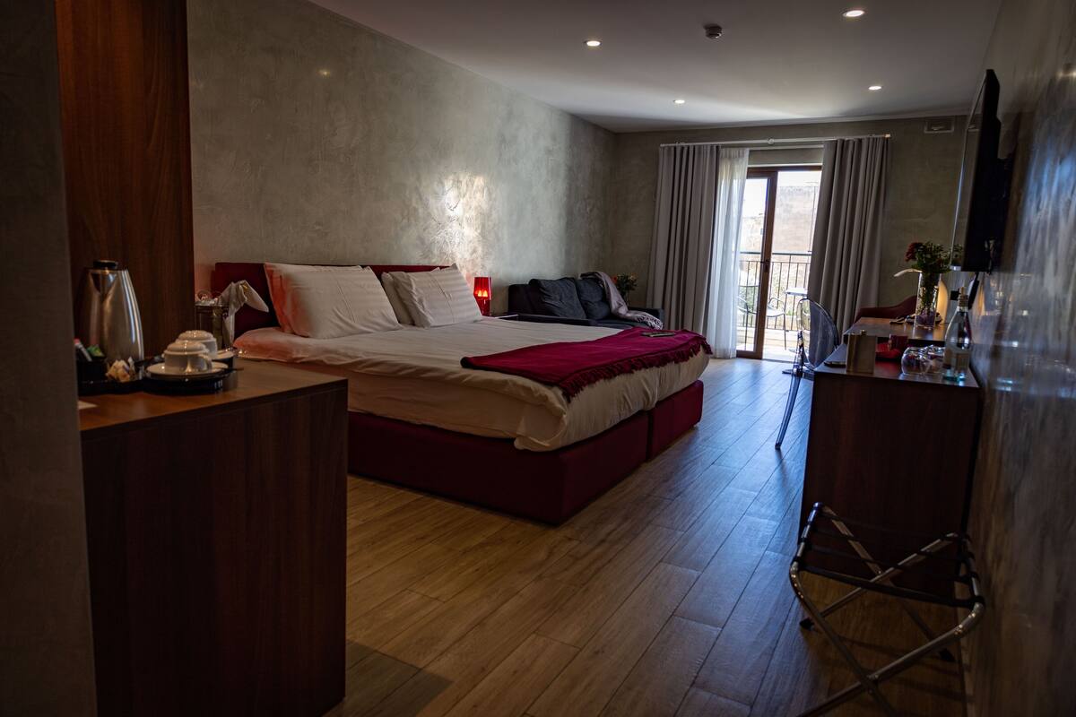 A modern hotel room with a large bed, a desk, and a balcony with curtains.