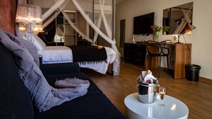 Quarto com cama, mesa de cabeceira com luminária, escrivaninha com cadeira e televisão na parede.