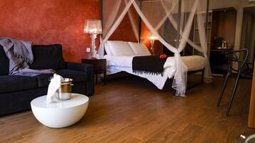 A bedroom with a four-poster bed, a sitting area with a sofa and a coffee table, and a bedside table with a lamp.