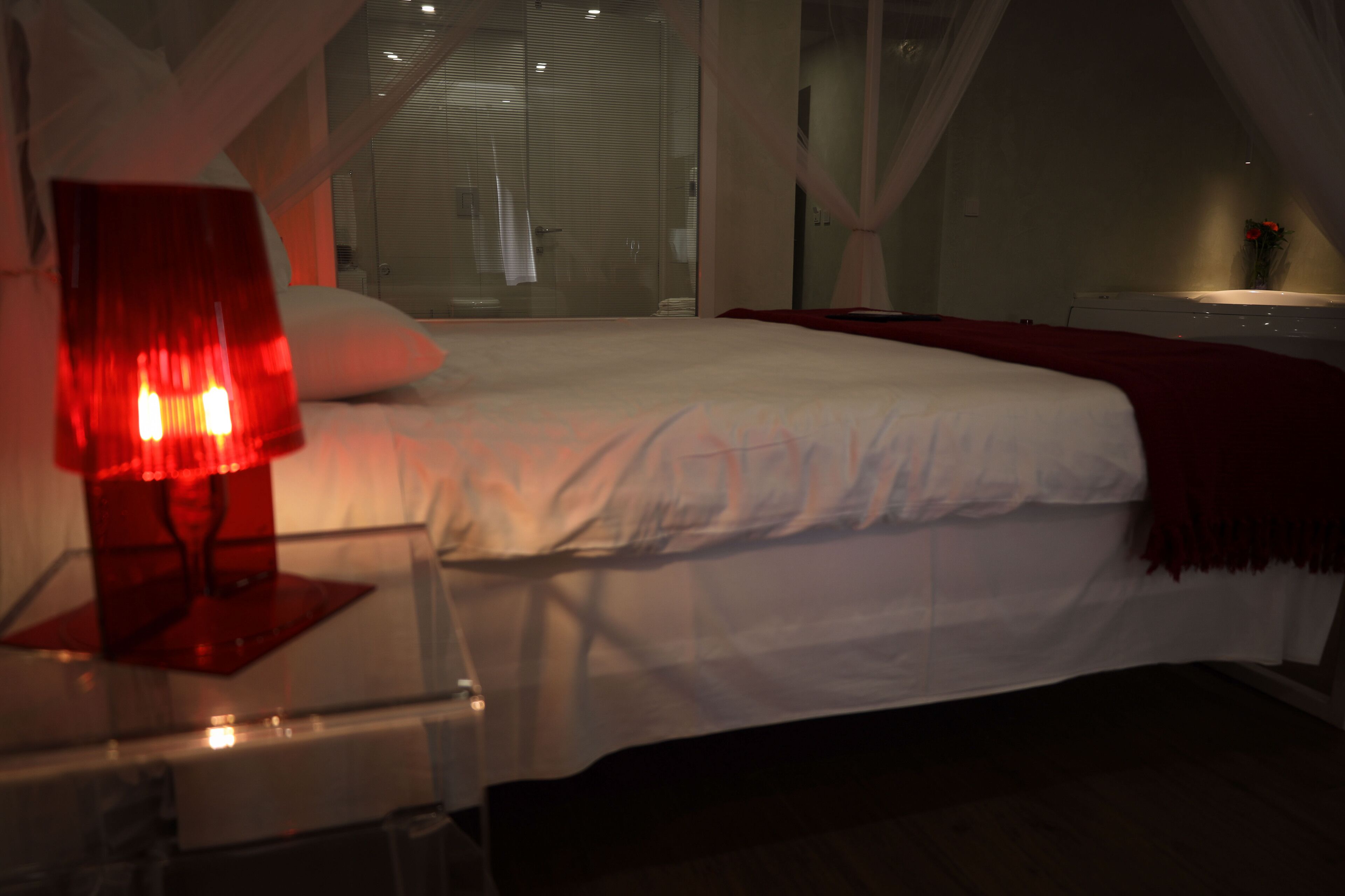 Un dormitorio con cama, una mesita de noche con lámpara y una ventana con cortinas.