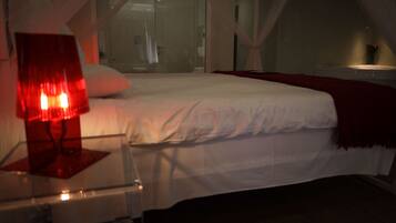 Un dormitorio con cama, una mesita de noche con lámpara y una ventana con cortinas.