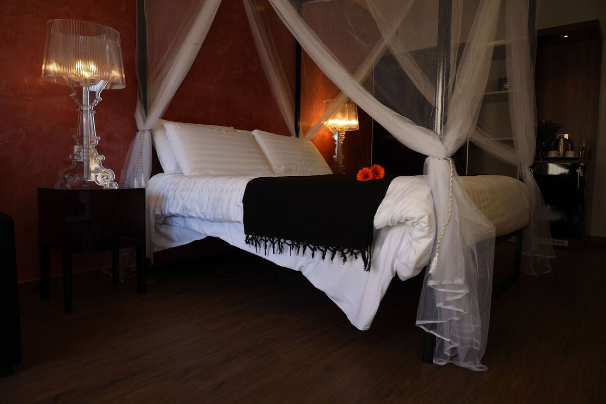 A bedroom with a four-poster bed, a bedside table with a lamp, and a nightstand.