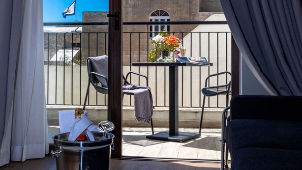 Uma varanda com vista para um edifício histórico, uma mesa com flores e uma cadeira moderna.