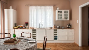 Una cocina con armarios blancos, una mesa de comedor con mantel de encaje y una ventana con cortinas de gasa.