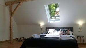 Un dormitorio con tragaluces, una cama con almohadas, una mesita de noche y un taburete pequeño.