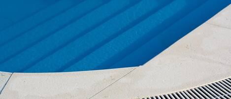 Una piscina con superficie azul cristalina, borde de concreto y una rejilla metálica en el fondo.