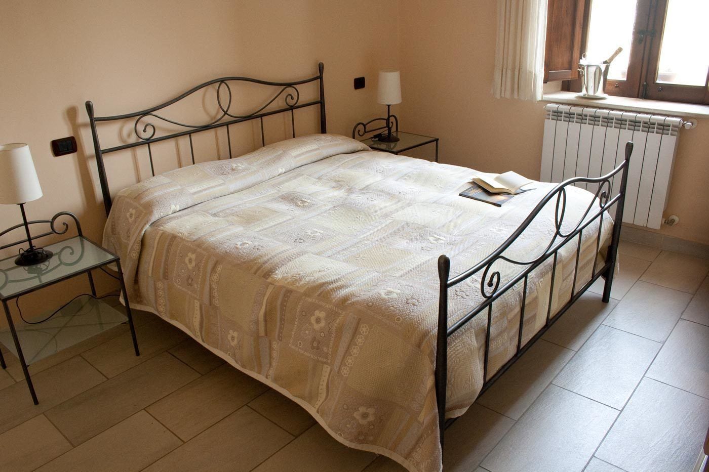 Una cama individual con una colcha estampada, una mesita de noche con una lámpara y un radiador en la esquina.