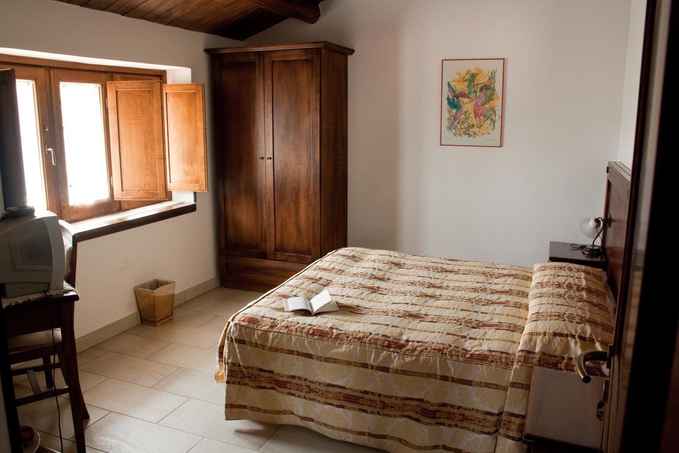 Un dormitorio con una cama, armario de madera, un escritorio con ordenador y una ventana.