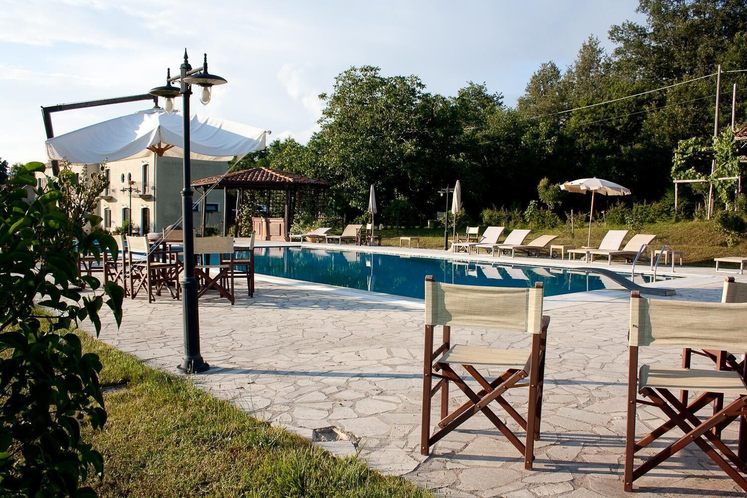 A pool area with lounge chairs, a pergola, and a building with a tiled roof.
