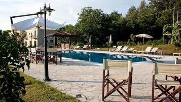 A pool area with lounge chairs, a pergola, and a building with a tiled roof.