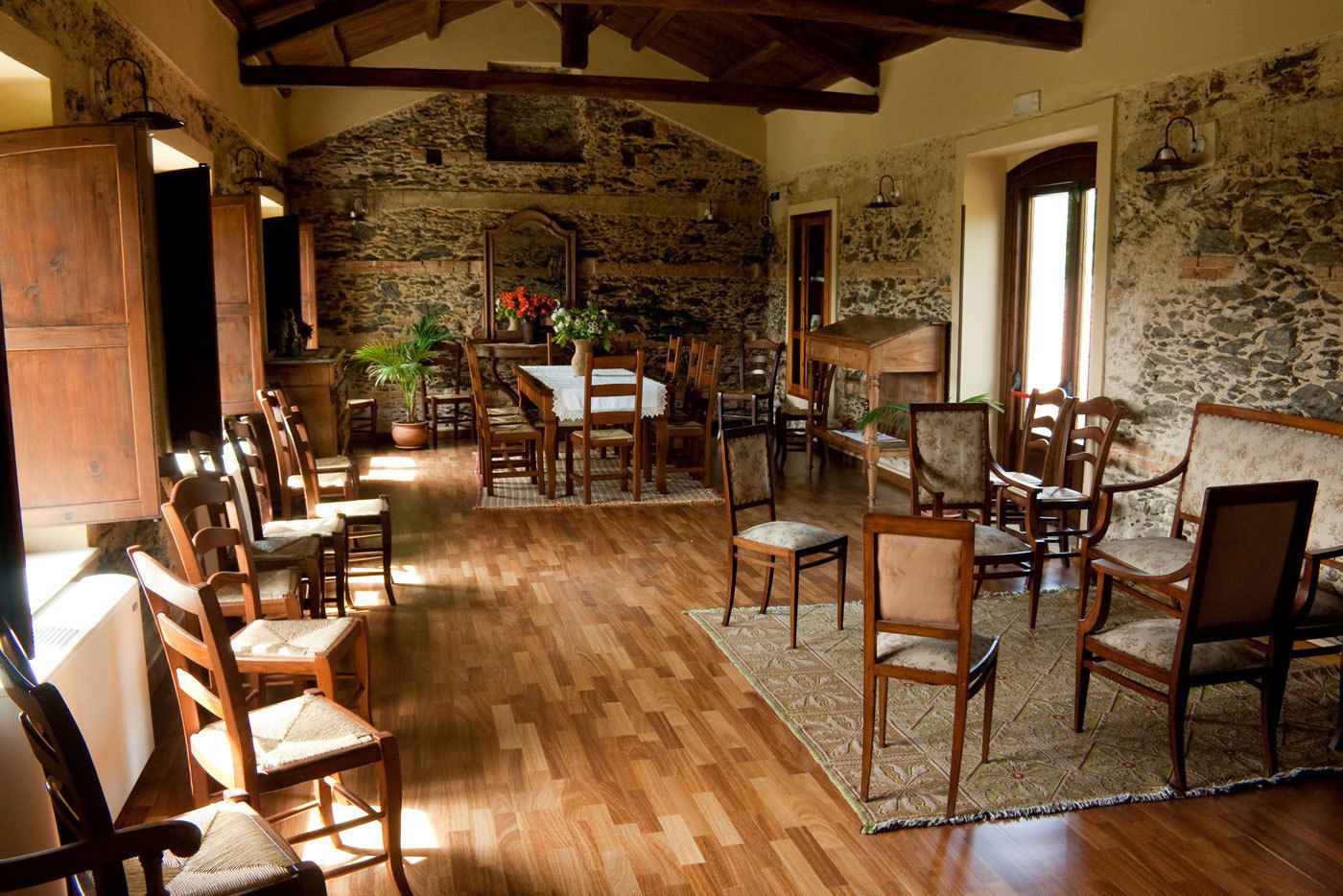 A rustic dining area with wooden chairs and tables, stone walls, and a wooden ceiling.