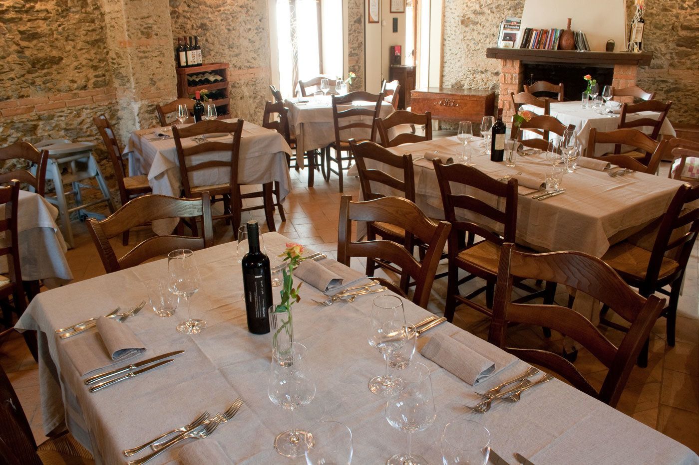 A restaurant with multiple tables set for dining, each with wine glasses, cutlery, and a bottle of wine.