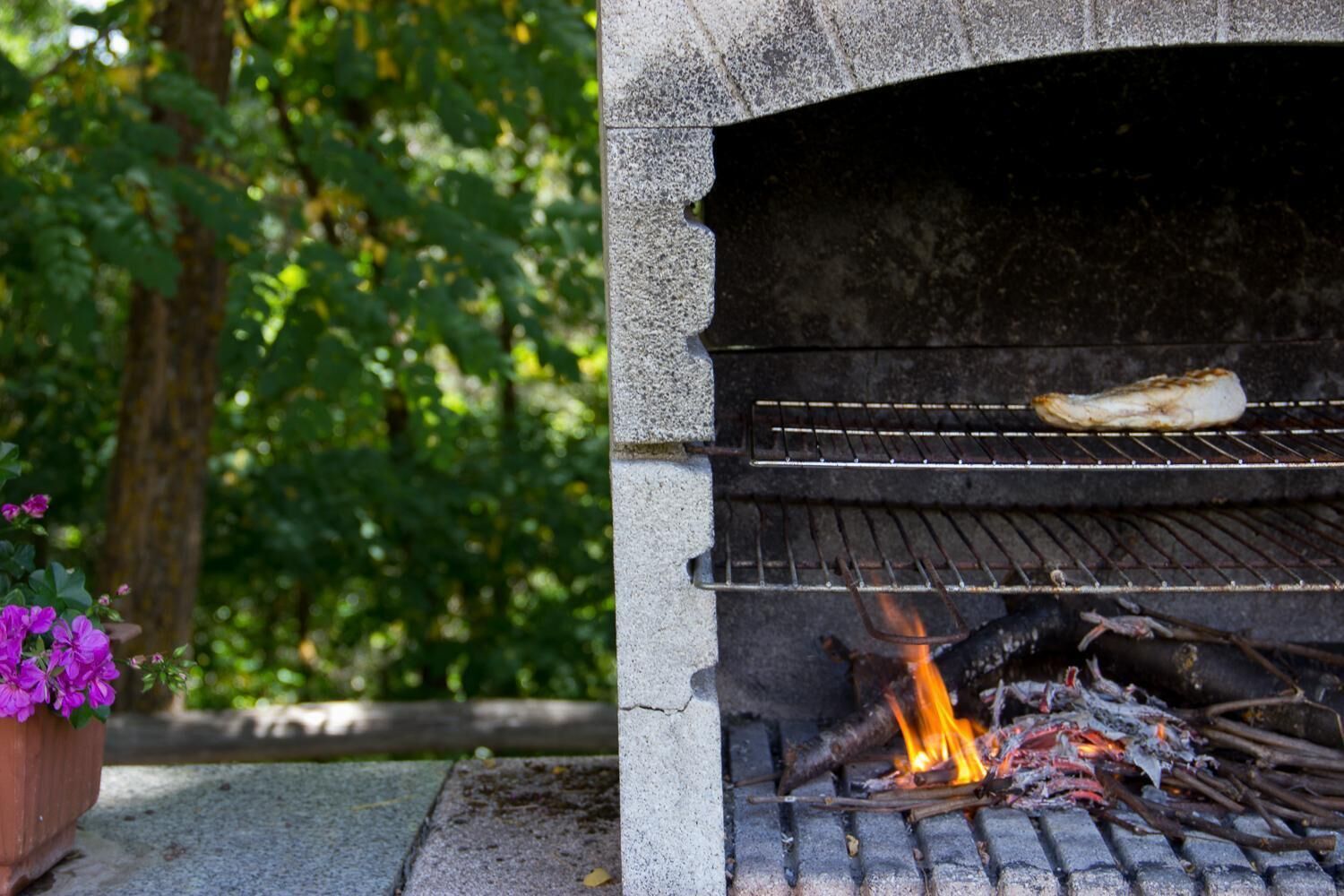 Un barbecue extérieur en pierre, avec un morceau de viande en train de cuire sur la grille supérieure et des flammes en dessous.